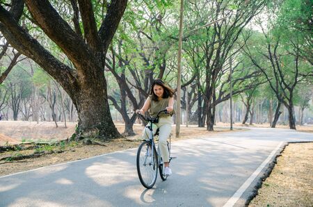 asian girl is riding bicycle on road in park with smile faceの写真素材