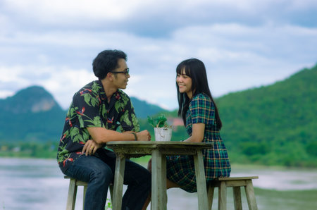 Asian couple are sitting on chair with table on mountain and river background with smile face