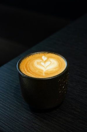 hot latte art coffee with heart mug in black cup on black tableの写真素材