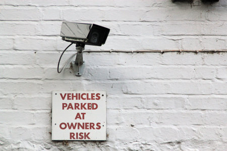 Sign for \\\\\\\Vehicles parked at owners risk\\\\\\\ on a white brick wall and a CCTV camera...