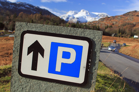 Close up of a parking sign against a backdrop of country roads, lush countryside and snow-capped mountains symbolizing vacations in the countryside, hill walking and skiingの写真素材