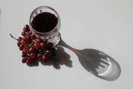 Glass of red wine and a bunch of red grapes in the sun with the shadow of the crystal wine glass symbolizing wine drinking, summer and al fresco eatingの写真素材