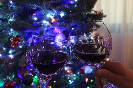 Luxury crystal glasses clinking together in celebration in front of a Christmas tree with baubles and fairy lightsの写真素材