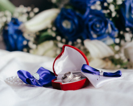 Wedding rings in a red box with a blue bow.の写真素材