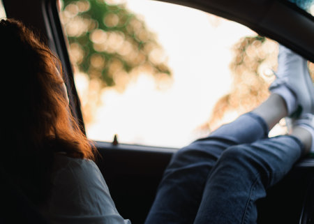 Close-up of a young woman sitting in the back seat of a car and looking out the windowの写真素材