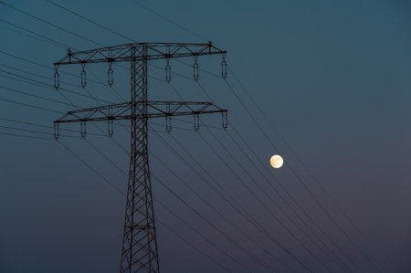 High Voltage Electric Transmission Tower Energy Pylon and Full Moon at Duskの写真素材