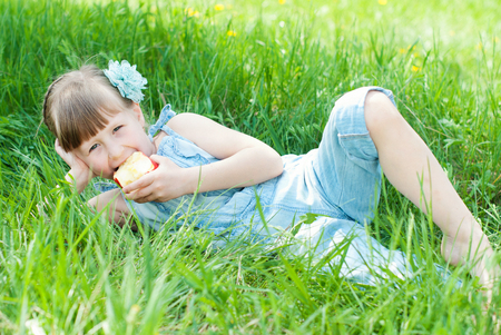 Pretty girl eating red apple on grassland. Happy kids concept. Healthy lifestyle, healthy eatingの写真素材