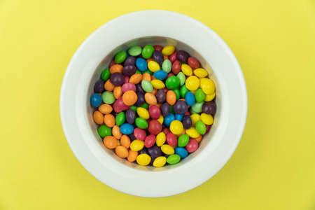 White round plate on a yellow background full of multi-colored sweetsの写真素材