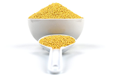 White bowl with a white spoon on a white background with a hill of millet groats. Studeio shot.