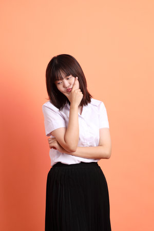 Cheerful female student in Thai university uniform with gesture of thinking isolated on orange background. International Students' Day, World Students' Day. Gen Zの写真素材