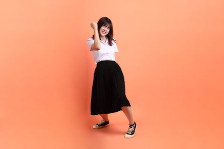 Cheerful female student in Thai university uniform with gesture of cheerful, excited, celebrating isolated on orange background. International Students' Day, World Students' Day. Gen Zの写真素材