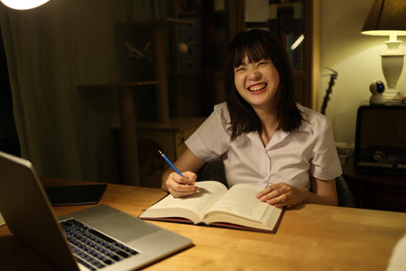 A young female student in a Thai university uniform sits at a desk in study, doing homework and study hard. International Students' Day, World Students' Day. Gen Z, E-learningの写真素材