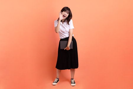 Cheerful female student in Thai university uniform with gesture of holding a textbook isolated on orange background. International Students' Day, World Students' Day. Gen Zの写真素材