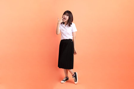 Cheerful female student in Thai university uniform with gesture of multiple posing isolated on orange background. International Students' Day, World Students' Day. Gen Zの写真素材
