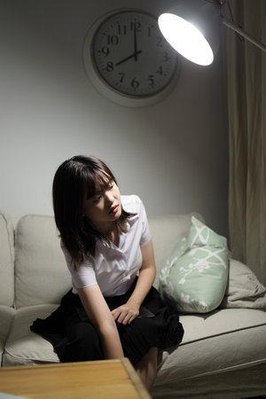 A young female student in a Thai university uniform sits on a sofa in the living room, Waiting for her parent. International Students' Day, World Students' Day. Gen Zの写真素材