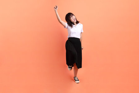 Cheerful female student in Thai university uniform with gesture of cheerful, excited, celebrating isolated on orange background. International Students' Day, World Students' Day. Gen Zの写真素材