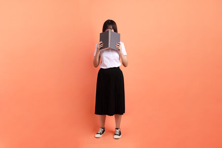 Cheerful female student in Thai university uniform with gesture of holding a textbook isolated on orange background. International Students' Day, World Students' Day. Gen Zの写真素材