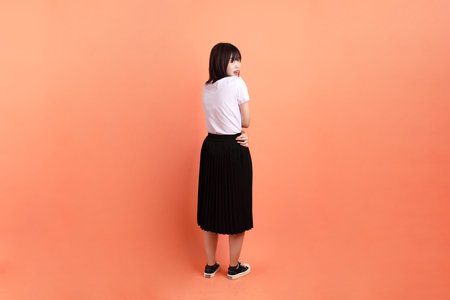 Cheerful female student in Thai university uniform with gesture of self love and care isolated on orange background. International Students' Day, rear view. Gen Zの写真素材