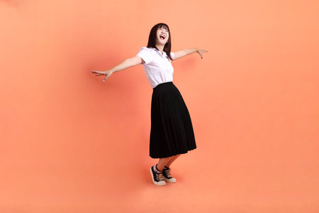 Cheerful female student in Thai university uniform with gesture of multiple posing isolated on orange background. International Students' Day, World Students' Day. Gen Zの写真素材