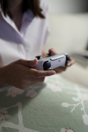 A young female student in a Thai university uniform sits on a sofa in the living room, playing video games. International Students' Day, Gen Zの写真素材