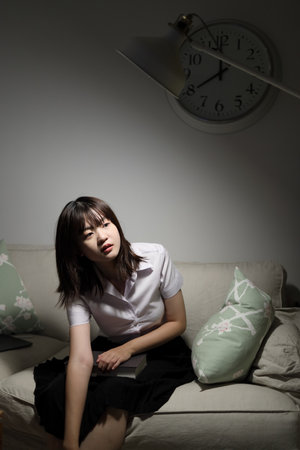 A young female student in a Thai university uniform sits on a sofa in the living room, Waiting for her parent. International Students' Day, World Students' Day. Gen Zの写真素材