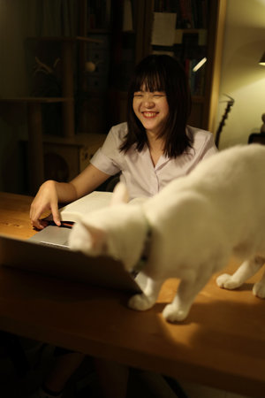 A young female student in a Thai university uniform sits at a desk in study, interacted with White Khao Manee cat. Animal and human interaction.の写真素材