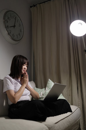 A young female student in a Thai university uniform sits on a sofa in the living room, studying online with a laptop. International Students' Day, World Students' Day. Gen Z, E-learningの写真素材