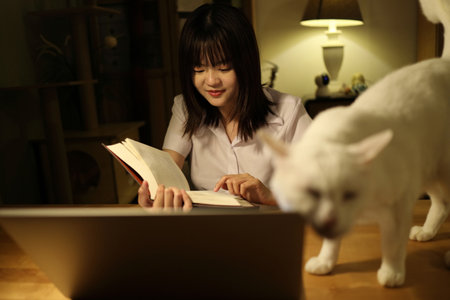 A young female student in a Thai university uniform sits at a desk in study, interacted with White Khao Manee cat. Animal and human interaction.の写真素材