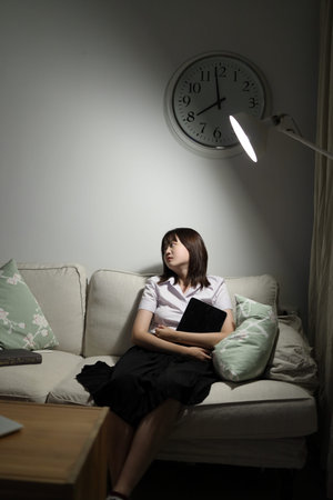 A young female student in a Thai university uniform sits on a sofa in the living room, Waiting for...