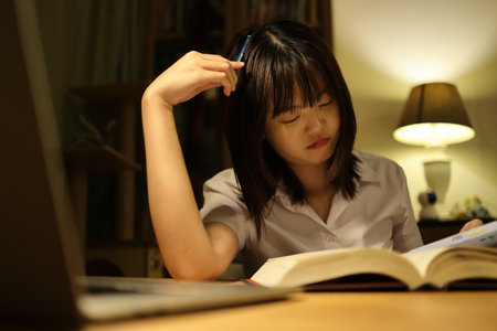 A young female student in a Thai university uniform sits at a desk in study, doing homework and study hard. International Students' Day, World Students' Day. Gen Z, E-learningの写真素材