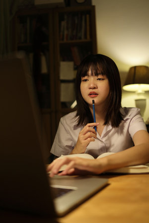 A young female student in a Thai university uniform sits at a desk in study, studying online with a laptop. International Students' Day, World Students' Day. Gen Z, E-learningの写真素材