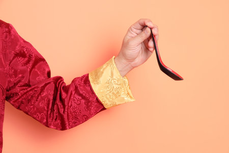 Happy Chinese new year. Hand of asian chinese senior man wearing red traditional clothing with gesture of hand holding spoon isolated on orange background.の写真素材