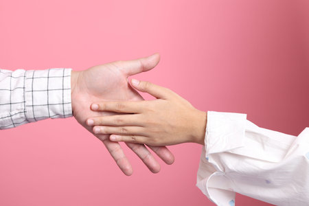 Close up hands of asian male and female showing gestures of Handshake isolated on pink background.