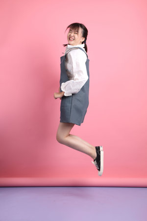 Cheerful lovely young asian woman in overalls casual clothes with gesture of jump isolated on pink...