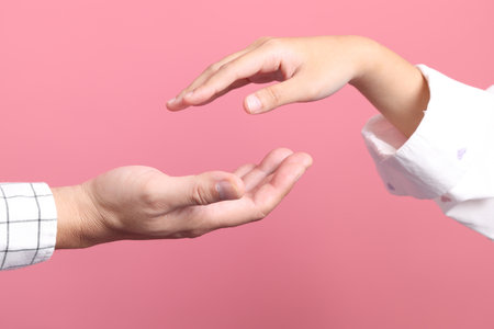 Close up hands of asian male and female showing gestures to protect, insurance, and security in life and property isolated on pink background.の写真素材