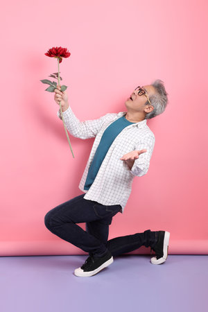 Asian senior man in casual clothing with gesture of holding a bouquet of flowers isolated on pink background. St Valentine's Day, Women's Day, Birthdayの写真素材