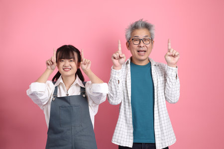 Asian senior man and woman couple in overalls casual clothing with gesture of pointing and greeting isolated on pink background. St Valentine's Day, Women's Day, Birthdayの写真素材