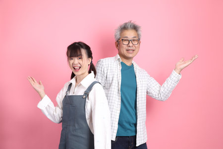 Asian senior man and woman couple in overalls casual clothing with gesture of pointing and greeting isolated on pink background. St Valentine's Day, Women's Day, Birthdayの写真素材