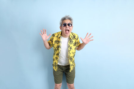 HAPPY SONGKRAN DAY. Asian tourist senior man in summer clothing with gesture of  surprise isolated on blue background. Songkran festival. Thai New Year's Day.の写真素材