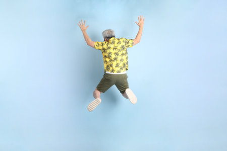 HAPPY SONGKRAN DAY. Asian tourist senior man in summer clothing with gesture of  jumping isolated on blue background. Songkran festival. Thai New Year's Day.の写真素材