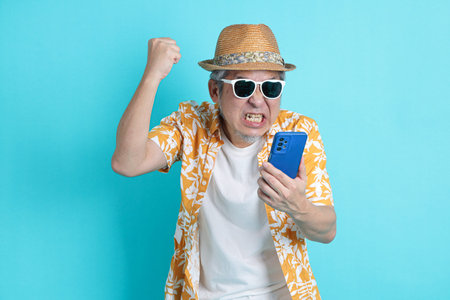 Portrait of Asian energetic senior man holding a mobile phone isolated on the blue background with...