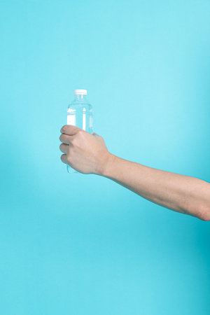 Asian man's hand holds bottle of water or transparent plastic bottle, isolated on  blue background. White cap, Close up.の写真素材