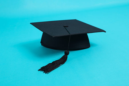 Black Graduation cap or Mortarboard with black tassel isolated on blue background.