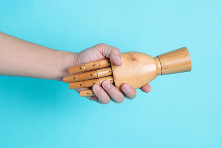 Hand of mannequin shake hands with human hand on isolated blue background. Symbol, teamwork.の写真素材