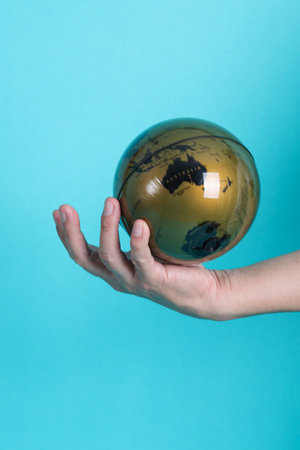 Humanâ€™s hand holding a globe on isolated blue background.