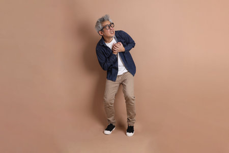 Portrait of Asian energetic senior man holding a mobile phone isolated on the blue background with travel clothes. mature man, Asian man. Elderly, Holiday, Travel. studio shot. Multiple emotions.の写真素材