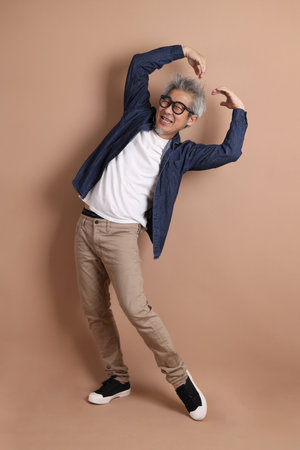 Asian energetic senior man with glasses posing  isolated on the brown background with casual clothes. mature man, Asian man. Elderly,  studio shot. Multiple emotions.の写真素材