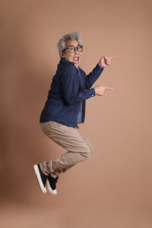 Asian energetic senior man with glasses posing  isolated on the brown background with casual clothes. mature man, Asian man. Elderly,  studio shot. Multiple emotions.の写真素材