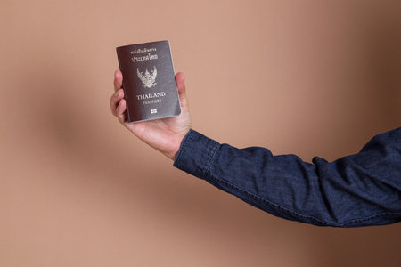 A asian man hand holding passport on blue background. Male with travel document. Identity, nationality verification.の写真素材