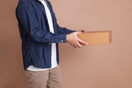 Asian man holding a box, concept of delivery, shopping or business, brown backgroundの写真素材